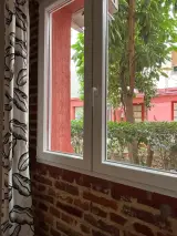 Ventana del dormitorio con alféizar de ladrillo y vistas al jardín con árboles y edificio rojo